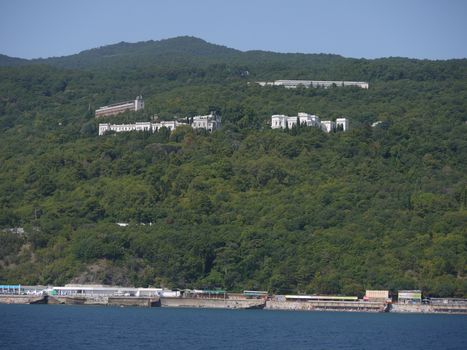 Green mountain slopes covered with dense forest with peeping roofs of houses. The seaside with the beach below.