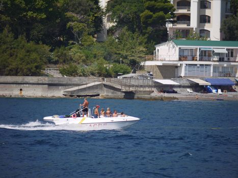 the motor boat dissects the blue sea waves against the back of the waterfront with buildings