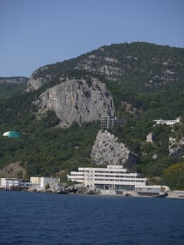Coast with rocky mountains with greenery. On it there is a luxurious villa with a view of the open sea