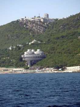 Round architectural building of the sanatorium on the background of the beach with vacationers and the boundless blue sea
