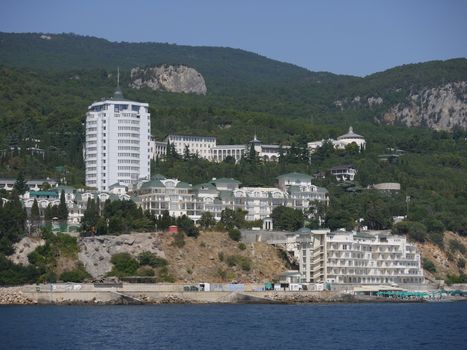 A beautiful hotel complex with a green roof against the backdrop of green rocky mountains and the blue sea