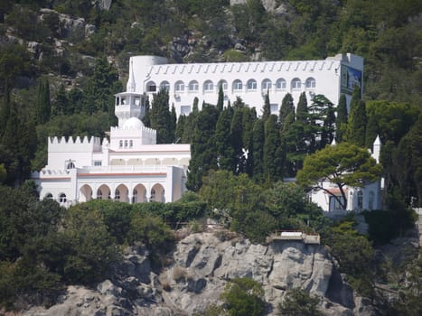 A beautiful snow-white palace with a spire on the tower is located between the greenery on the rock