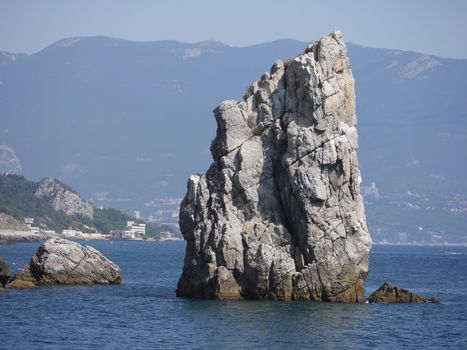 steep rock in the middle of the sea against the backdrop of the mountains