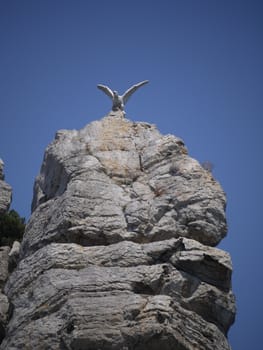 stone statue of an eagle on a high, steep rock under the blue sky