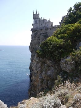 A dark, blue, calm sea with a rocky shore and a tower on one of the rocks