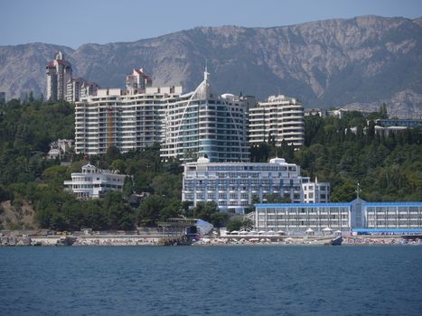 The sea with the beach and vacationers on it. With luxurious buildings of hotels standing on a mountainside among beautiful nature.