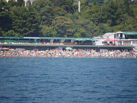 a huge number of vacationers on the beach by the sea at the foot of the mountain with the hotel