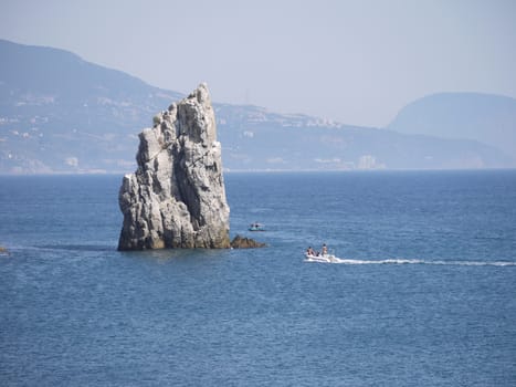 a tall rocky promontory in the sea against the backdrop of a cloudy, distant coastline