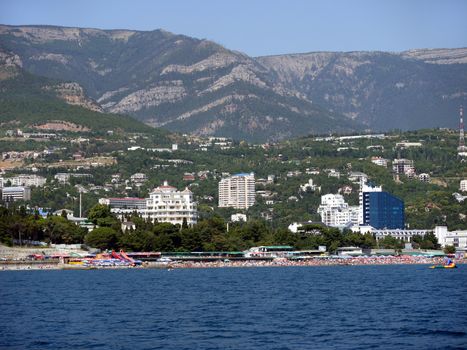 The sea beach is crammed with tourists with a beautiful view behind them to the city with a developed resort infrastructure with many hotels.