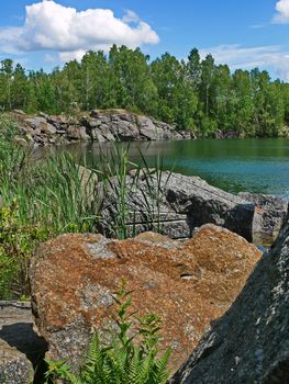 The shore of the lake with large granite cobblestones. Many of them are covered with brown-red slag. Most likely it is oxidized by the metal present in them