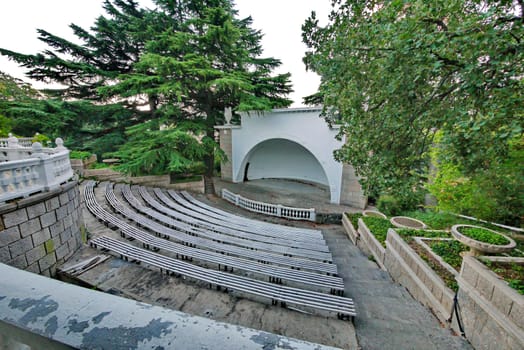 a small scene of a street theater with wooden benches in the botanical garden