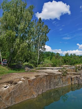 stone pond shore against the background of birches and clouds