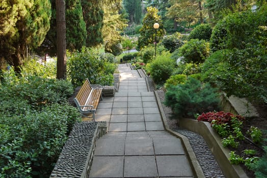 A staircase with steps and flower beds around, among the green park, and around are lanterns