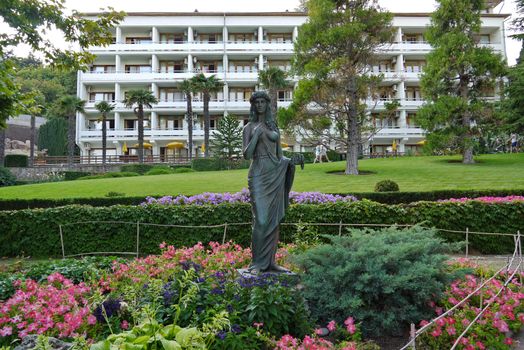 Monument to a beautiful woman standing among the flower bed and as if admiring the multicolored flowers