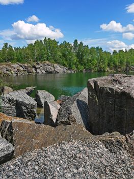 rocky shores of a lake near a forest on a background of blue sky with clouds