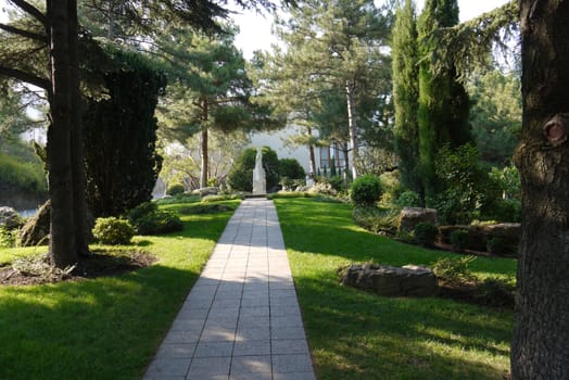 A tiled walkway with green trees on either side leading to a stone sculpture