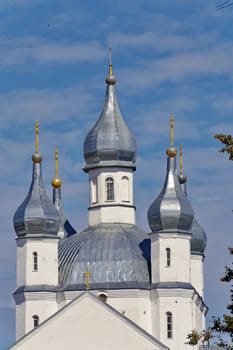 The roof of the church with white turrets and glistening domes with crosses is located on the background of a blue sky with transparent clouds.