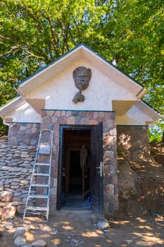 a stone wall of a small building with a wall-mounted pedestal of a man's face at the entrance