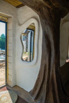 A window of unusual shape in the wall of the building overlooking the street on a building composed of multi-colored stones.