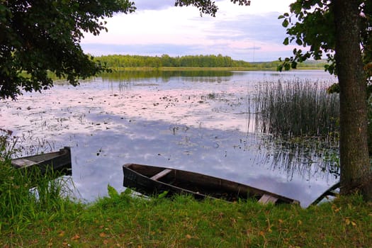 Old wooden boats at the shore of a small transparent lake against a background of deciduous forest