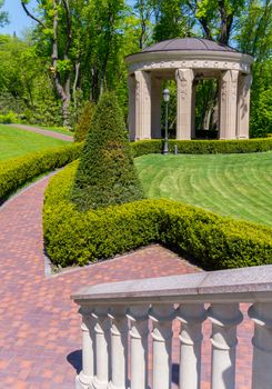 concrete gazebo with columns under the dome in a green well-groomed park near the alley