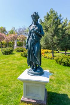 Metal sculpture of a woman in antique style on a white stand on a green lawn