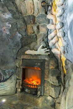 A fireplace made in the wall made of stone. With an unusual setting, the model of a hand lying on it and an unusual stucco on the wall next to it.