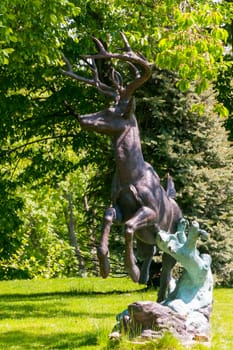 An interesting statue of a small deer with branched horns preparing to jump standing in a park in the shade of a tree.