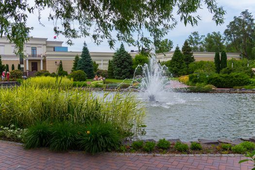 people resting on a bench near a pond with a fountain in the middle of it