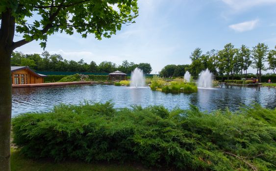 Several beautiful fountains in the middle of the lake on the background of a wooden building and a gazebo for rest