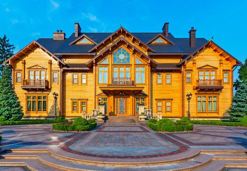 The path to the central entrance to a huge wooden cottage with wide balconies and a black roof