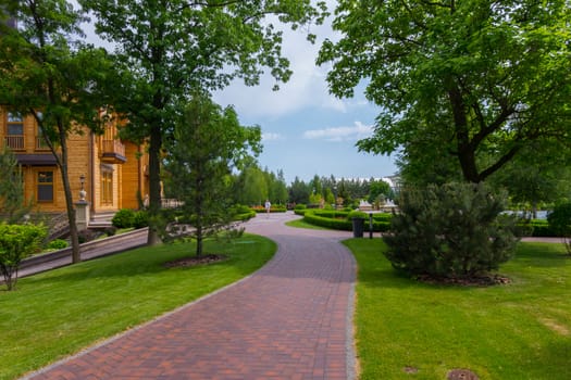 The park alley with a beautiful green lawn along it, leading to a luxurious wooden villa