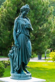 Bronze statue of a woman with a basket of flowers in the park on the background of a fluffy pine