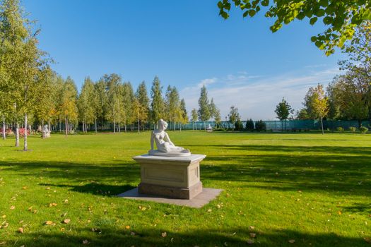 Sculpture of a naked girl against a neatly trimmed green lawn and small birches