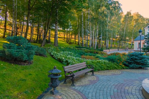 Wooden bench with wrought decorative railing against a background of a slope with flower beds