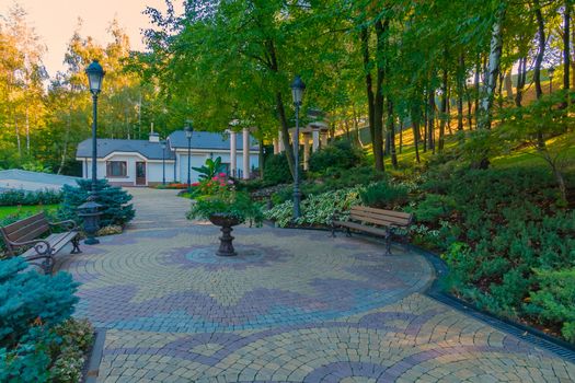 Alley overlooking the gazebo with columns and a flower bed of decorative flowers in the middle