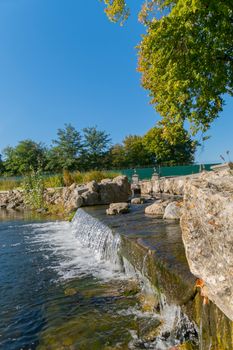 cascading waterfall with stone boulders along the banks, in a park under a tree. Mezhygir. Ukraine