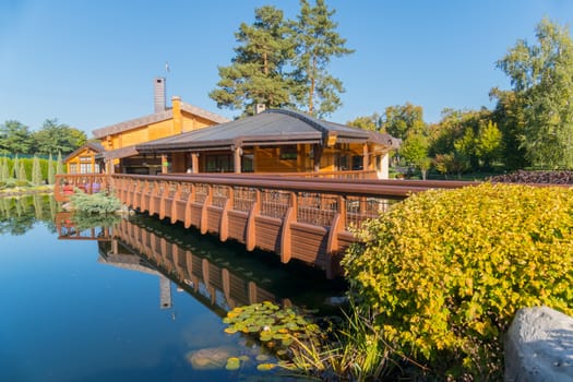 A beautiful bridge of wood passing over a pond in the park leading to a beautiful view of the cafe with a summer terrace.