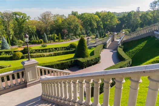 The stairs in the park are located on the slope connecting with each other paths with growing shrubs growing on the side of them.