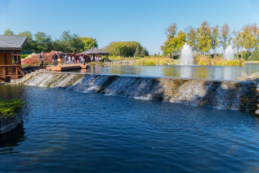 Tourists watch and photograph a small decorative waterfall flowing from one lake to another