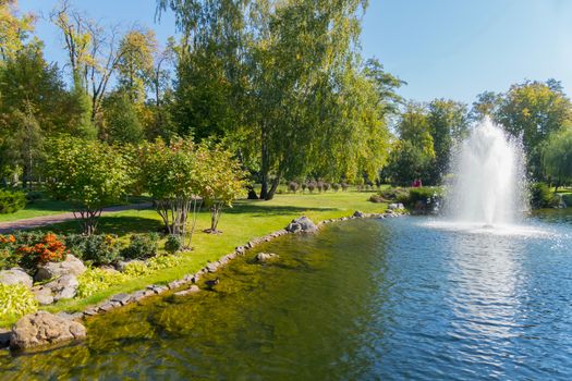 well-groomed green lawns in the shade of trees on the shore of a pond lined with a stone with clear water