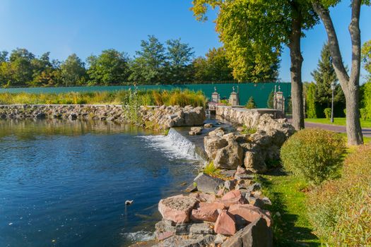 Beautiful blue transparent lake with small decorative waterfalls in the background of the park zone
