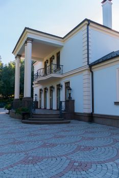 Entrance to a two-storey building with white columns and high windows. Around on the ground a tile with a floral pattern