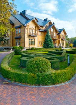 A flowerbed with a labyrinth of green bushes near the chic wooden mansion