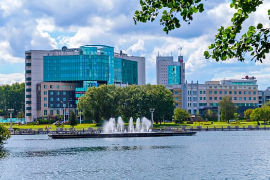 A chic landscape of a pond in the city with beating fountains located on the background of a modern business center building.