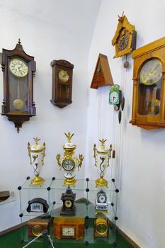 many gorgeous antique watches hanging on the white wall and standing on the bottom of the glass case