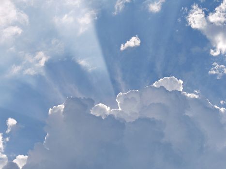 the rays of sunlight break through between the edges of a fluffy white cloud on a blue sky