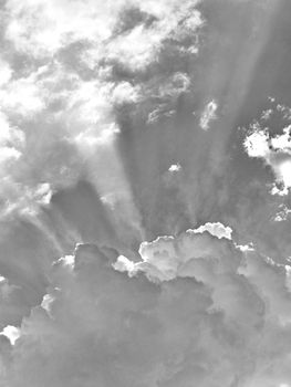 A photo of the sky in the clouds through which the sun's rays break through in a black and white filter