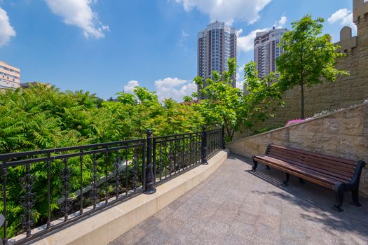 A bench for rest standing on a viewing platform in a cozy place near the tops of green trees with a beautiful view of the city houses against the background of clouds.
