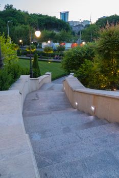 Steps in the park leading down with lanterns standing on each side for lighting in the dark with resting downstairs on the bench by people standing on the mall.